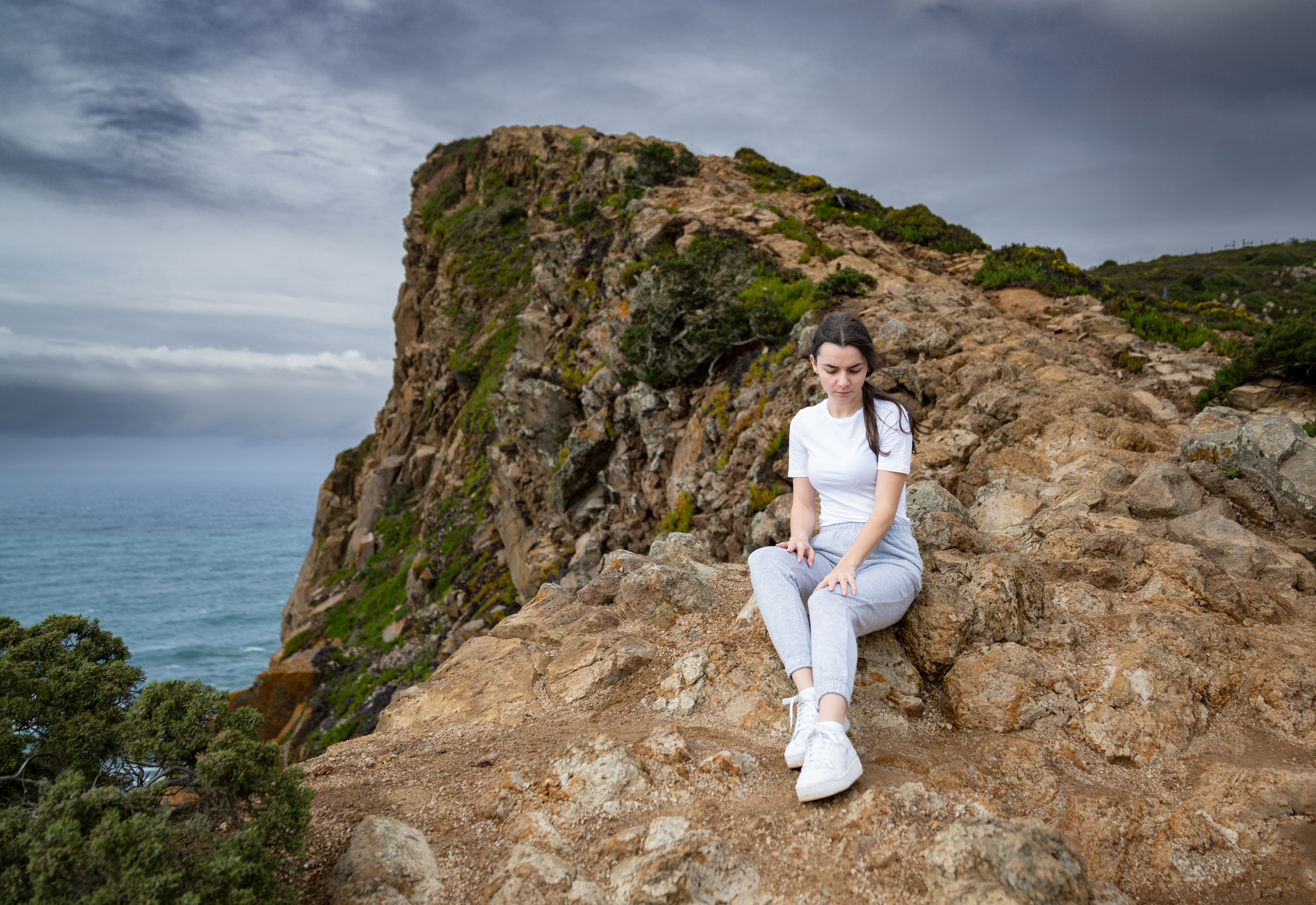 young woman sitting on coastal cliff edge scenic s 4cbcf0c6e92094271430 BTOURS
